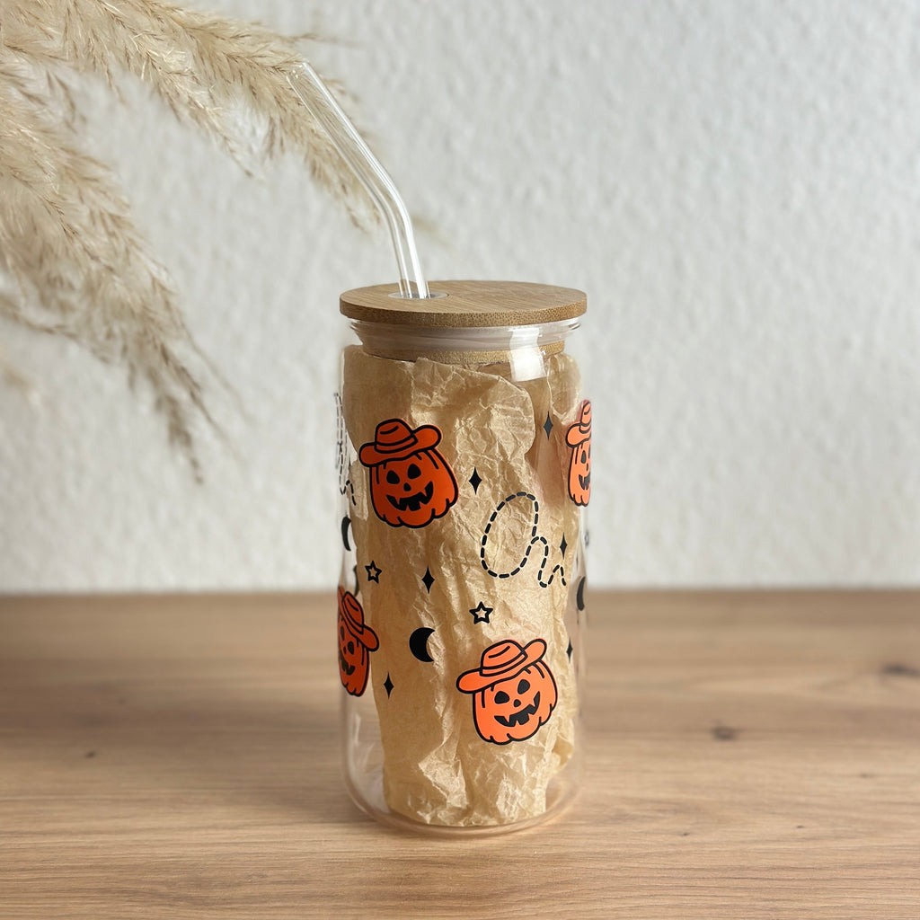 Glasbecher mit Kürbis-Geister-Halloween-Design in Orange und Weiß, Bambusdeckel und Glasstrohhalm, 500 ml Matcha-Glas vor Pampasgras von Momentwerk Studio