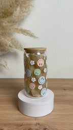 Glasbecher mit Smiley-Blumen-Design in bunten Pastelltönen, Bambusdeckel und Glasstrohhalm, 500 ml nachhaltiger Trinkbecher von Momentwerk Studio in der Rundum-Ansicht